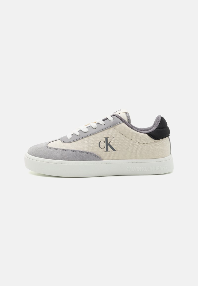 Tenisky Calvin Klein s béžovou plátnovou svrchní částí a šedou semišovou patou, kulatou špičkou, bílými tkaničkami, černými akcenty na patě a logem na boku.