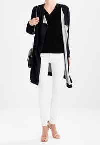 Lungo cardigan blu navy con interno grigio chiaro, sopra una maglietta nera e pantaloni bianchi. Accessoriato con una borsa nera e sandali color carne.