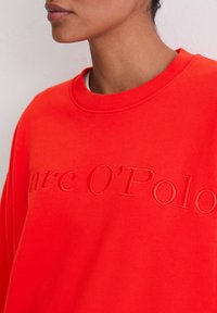 Czerwony sweter z teksturą, haftowanym logo "Parc O'Polo." Posiada okrągły dekolt oraz luźny krój z prążkowanymi detalami.