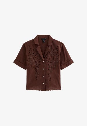 Camisa marrón de manga corta con botones, bordado floral y dobladillo con borde festoneado, que presenta un cuello con muesca y tela ligera.