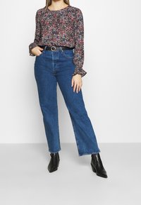 Blus med blommönster och långa ärmar i blått, rött och vitt, tillsammans med högmidjade blå denimjeans. Svart bälte med rund silverspänne och svarta ankelboots.