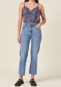 Floral-patterned sleeveless top in dark blue with a V-neckline, paired with high-waisted light blue straight-leg jeans and black loafers.