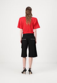 Rode top met korte mouwen en een relaxte pasvorm, gecombineerd met zwarte cargoshorts tot de knie met ritszakken. Het model draagt zwarte hoge hakken.
