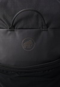Svart ryggsekk laget av teksturert stoff, med et rutemønster, topphåndtak og en subtil logo av en mammut preget på fronten.
