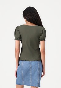 Top a coste verde oliva con maniche a sbuffo corte, orlo e polsini con bordo ondulato, abbinato a una mini gonna di denim blu con cuciture verticali.
