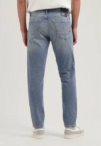 Jeans de mezclilla de color azul claro con corte recto, cinco bolsillos y un acabado desgastado. Parche de logo destacado en la cinturilla trasera.