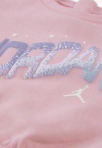 Różowa bluza z kapturem z wyraźnym napisem "JORDAN" w gradientowym niebieskim kolorze z ozdobnymi detalami, dopełniona białym logo Jumpman i akcentami gwiazd.