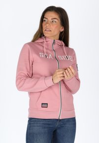 Felpa rosa con zip, cappuccio, tasche frontali e scritta 'SEA SIDE'. Tessuto morbido e polsini a coste. Piccolo logo ricamato in basso.