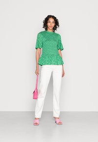 Top peplum verde com pregas e estampado floral branco, combinado com calças brancas, sandálias de bloco rosa e uma pequena mala rosa.