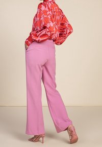 Blouse rouge à fleurs avec manches bouffantes, rentrée dans un pantalon large rose clair, associée à des sandales à talons roses. Finition en tissu lisse.