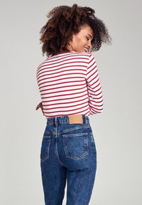 Chemise à rayures rouges et blanches à manches longues associée à un jean en denim bleu taille haute, avec un patch en cuir beige sur la ceinture.