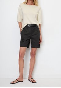 Sorte bomuldsshorts med en tætsiddende talje, parret med en cremefarvet, kortærmet striktop og sorte sandaler med stropper. Enkel design og farver.