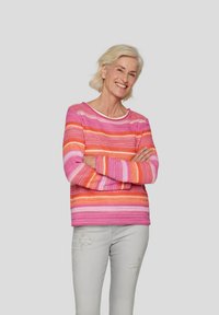 Bunt gestrickter Pullover mit horizontalen Streifen in Rosa- und Orangetönen, mit einem runden Ausschnitt und langen Ärmeln. Getragen mit hellgrauen Jeans.