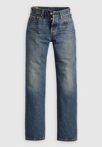 Jean en denim bleu à coupe droite, caractérisé par un effet délavé, des coutures apparentes et deux poches avant avec des éléments métalliques.