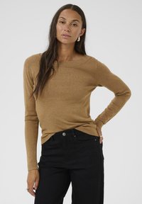 Maglietta a maniche lunghe color marrone chiaro in maglia con un ampio scollo, abbinata a jeans neri. La maglietta ha una texture morbida e un design aderente.