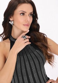 Top halter negru decorat cu cleme argintii. Modelul poartă cercei argintii și un inel metalic în formă de inimă în timp ce își atinge gâtul.