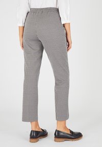 Schwarz-weiße Hahnentritt-Hosen mit elastischem Bund, schmalem Schnitt und knöchellangem Design, kombiniert mit schwarzen Loafers.