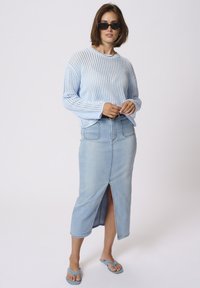 Light blue open-knit sweater with long sleeves, paired with a light wash denim skirt featuring a front slit and pockets. Worn with blue flip-flops.