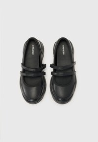 Zapatos negros con dos correas estrechas, hechos de un material sintético liso. Cuentan con una puntera redondeada y una suela acolchada con bordes texturizados.
