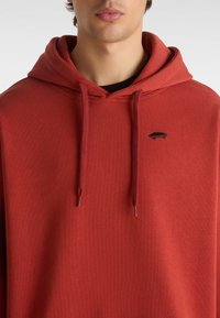 Roter Pullover-Hoodie aus weichem Material, mit einer vorderen Kängurutasche, Zugbändern und einem kleinen schwarzen gestickten Skate-Design.
