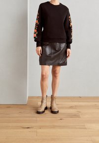 Černá mikina s barevnou květinovou výšivkou na rukávech, kombinovaná s černou koženou sukní a béžovými kotníkovými botami s černými podrážkami.