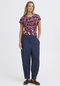 Rövid ujjú, mintás felső sötétkék, rózsaszín és fehér színekben, laza sötétkék nadrággal, az elején zsebekkel és gombos díszítéssel. Barna mokaszin.