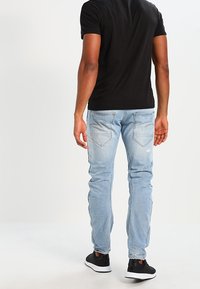 Ljusblå denimjeans med slim fit, med en blekt finish och två bakfickor. Kombinationen med en svart t-shirt med kort ärm och svarta skor.