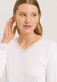 Bílé dlouhé rukávy tričko s výstřihem do V, zdobené jemným růžovým krajkovým lemem kolem výstřihu a rukávů. Hladký povrch a jednoduchý design.