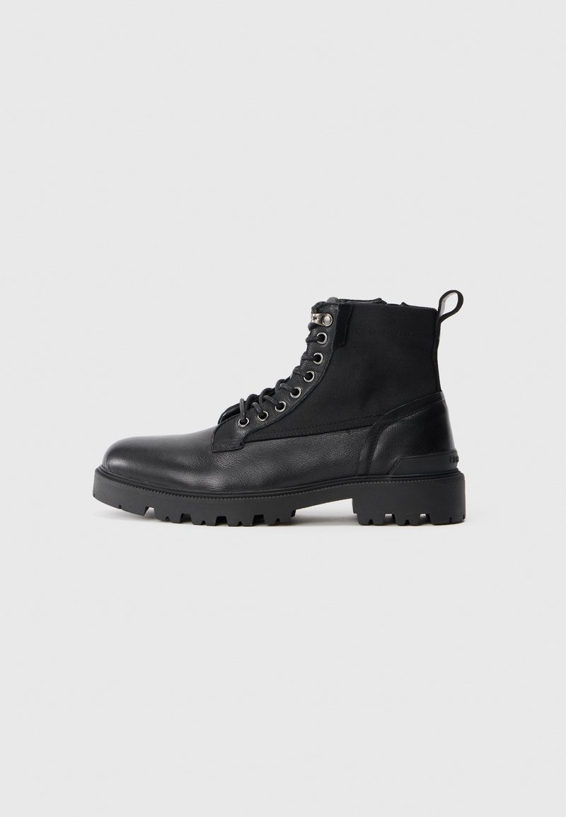 Stivaletto nero con lacci alla caviglia, suola robusta, punta e tacco in pelle, sezione superiore in tessuto e linguetta sul retro, su sfondo bianco.