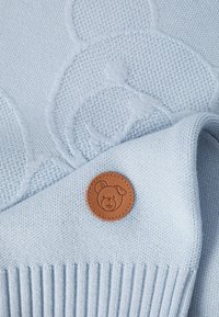 Heled sinine kudumine särk, millel on tekstuuriga karupattern ja nahkplekk, millel on karu näo embleem. Kortsutatud ääre disain.