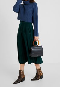 Kortsweater i blå ribbad stickning, grön veckad midikjol och ankelstövlar med ormskinnsmönster. Svart väska med bärnstenhandtag som accent.