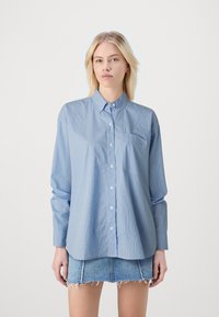 Svetlo modra srajca s dolgimi rokavi in navpičnimi belimi črtami, z žepom na prsih, v kombinaciji z uničenimi jeans krilom.