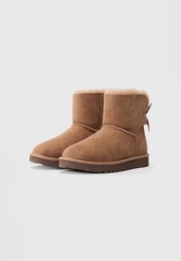Bottines en suede marron avec une doublure en fausse fourrure douce, bout rond et boucle d'accent à l'arrière. Semelle en caoutchouc texturée avec profil bas.