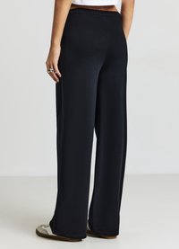 Pantalons larges noirs en tissu doux, dotés d'une taille élastique et d'une texture lisse. Le design notable inclut une silhouette épurée.