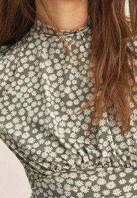 Groene bloemenjurk met witte madeliefjespatronen, geplooide textuur bij de halslijn en taille, gemaakt van een zachte, lichte stof.