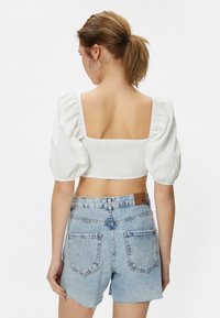 Weißes kurzärmliges, cropped Top mit quadratischem Rückenausschnitt, aus strukturiertem Stoff und mit puffigen Ärmeln, kombiniert mit zerrissenen Denim-Shorts.