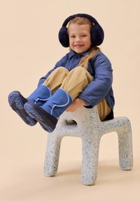 Blaue wasserdichte Winterstiefel mit einem weich gepolsterten Schaft, dunklen Sohlen, getragen von einem Kind, das auf einem strukturierten, gesprenkelten Kunststoffstuhl sitzt.