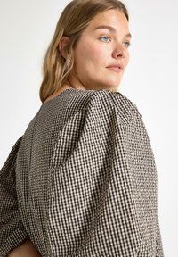 Svart och beige rutmönstrad blus med puffärmar, som har ett strukturerat tyg och en lös passform. Baksidan har en nyckelhålsdetalj.