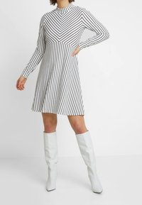 Svart och vit randig långärmad klänning med rund halsringning och utsvängd kjol, matchad med vita knähöga stövlar. Slät tygtextur.