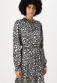 Robe noire et blanche à manches longues avec un motif d'étoiles, taille froncée et ourlet volanté. Présente un col à nouer et des manches à poignets.