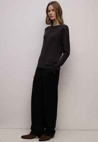 Donkere geribbelde top met lange mouwen en ronde hals, gecombineerd met loszittende zwarte broek en bruine suède enkellaarsjes.