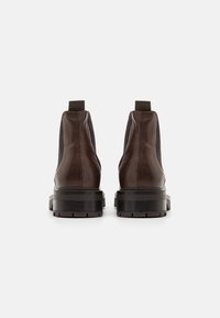 Botas chelsea de cuero marrón con paneles laterales elásticos y una suela de goma negra resistente. Presentan un acabado suave y un diseño de punta redonda.