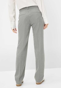 Grijze gestreepte broek met een losse pasvorm, voorzien van een platte tailleband en achterzakken, gecombineerd met een lichtgekleurde blouse en platte schoenen.