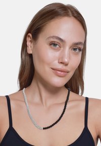 Collier accessoire avec des perles noires alternées et une section de chaîne argentée, présentant une texture lisse et des couleurs contrastées.