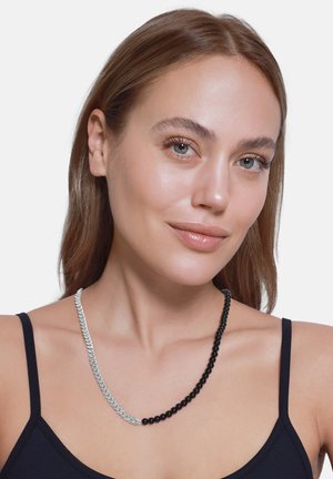 Collier accessoire avec des perles noires alternées et une section de chaîne argentée, présentant une texture lisse et des couleurs contrastées.