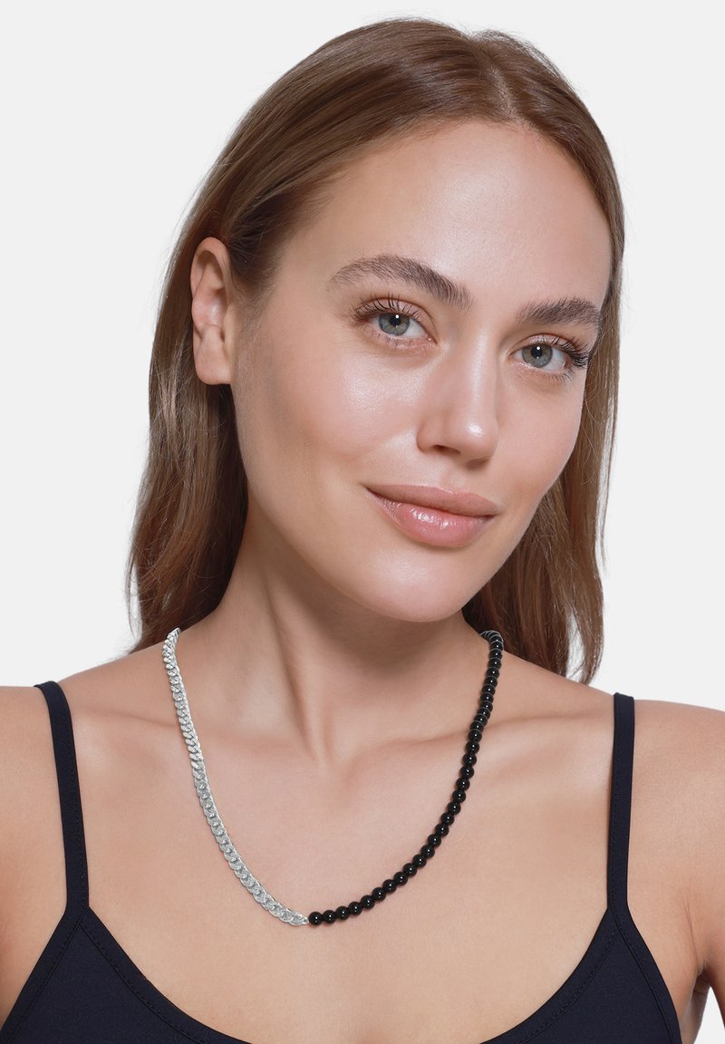 Collier accessoire avec des perles noires alternées et une section de chaîne argentée, présentant une texture lisse et des couleurs contrastées.