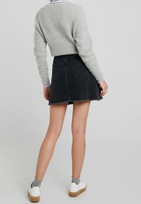 Svart denim mini kjol med fransat fåll. Kombinerad med en grå ribbad tröja och vita sneakers med bruna sulor, vilket visar en avslappnad stil.