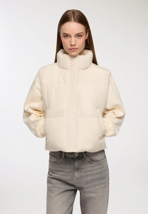 Giubbotto imbottito color crema con colletto alto, vestibilità oversize e polsini elasticizzati. Texture liscia, presenta pannelli cuciti e tasche laterali.