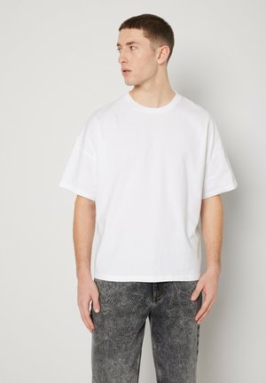White cotton T-shirt with a relaxed fit, crew neckline, and short sleeves, paired with gray denim jeans featuring a textured finish.