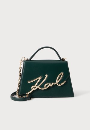 Sac à main trapèze vert foncé avec une poignée supérieure, une bandoulière chaîne dorée et un grand détail en écriture dorée "Karl" à l'avant.